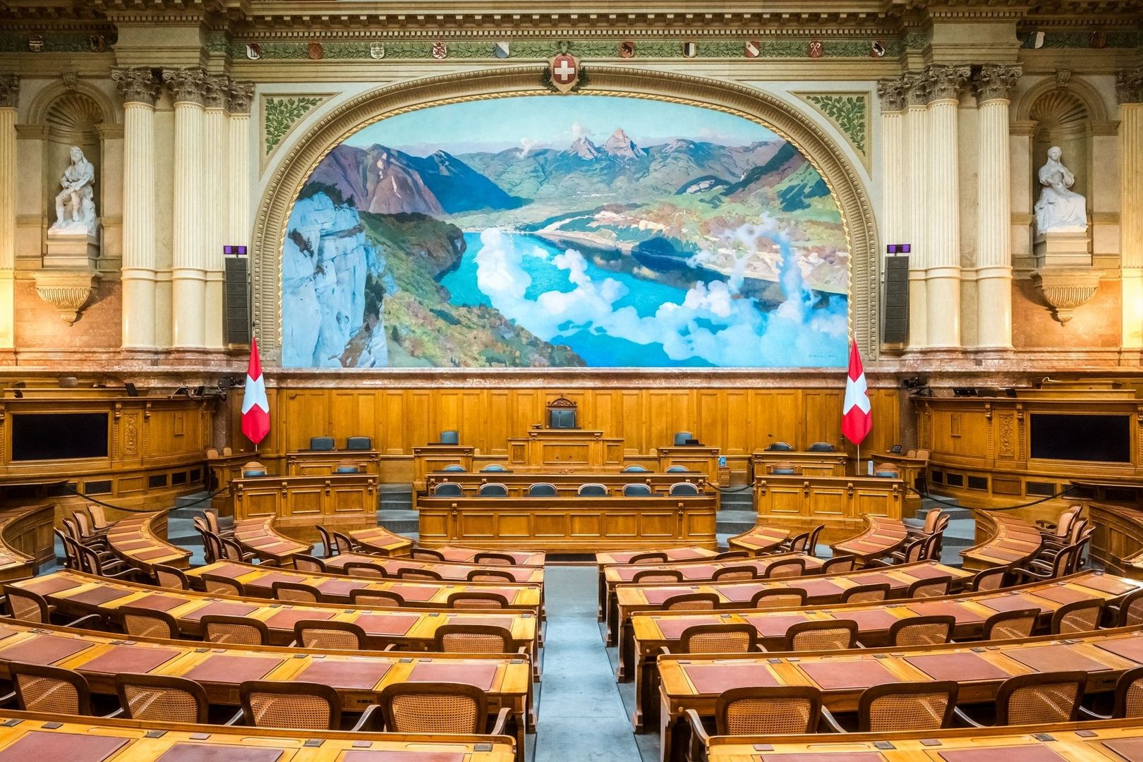 Empty Swiss parliamentary chamber with flags and Alpine mural