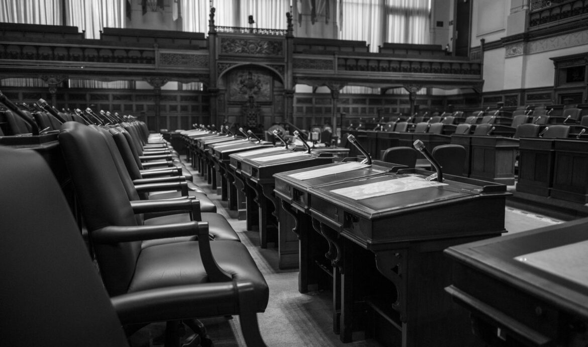 Empty parliamentary chamber with rows of desks, chairs, and microphones
