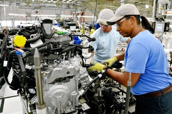 Two factory workers collaborate on an engine assembly line