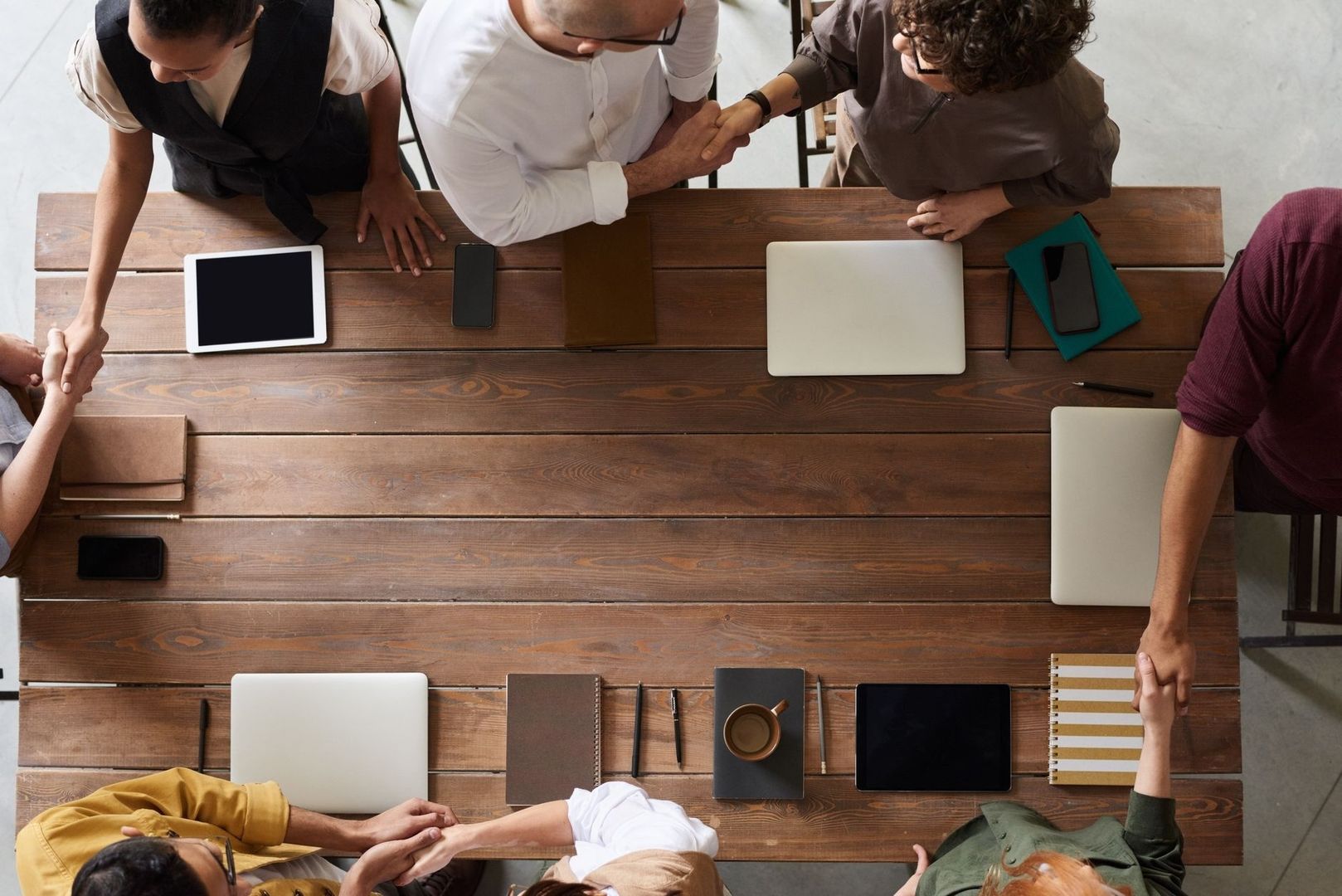 Overhead view of people shaking hands around a table with work devices